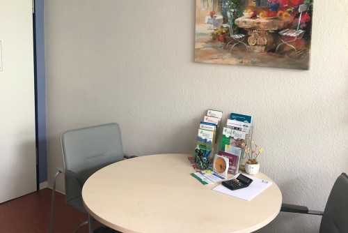 Beratungstisch mit 2 grauen Stühlen, buntes Bild an der Wand.