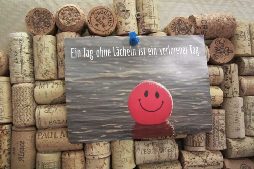 Jede menge Korken und eine Postkarte mit einem Smiley darauf und dem Spruch: Ein Tag ohne lächeln ist ein verlorener Tag.