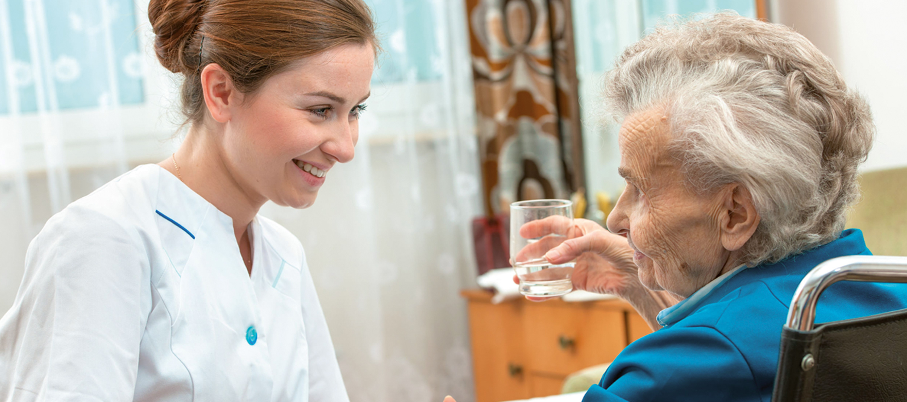 Eine Pflegekraft unterhält sich freundlich mit einer Seniorin.