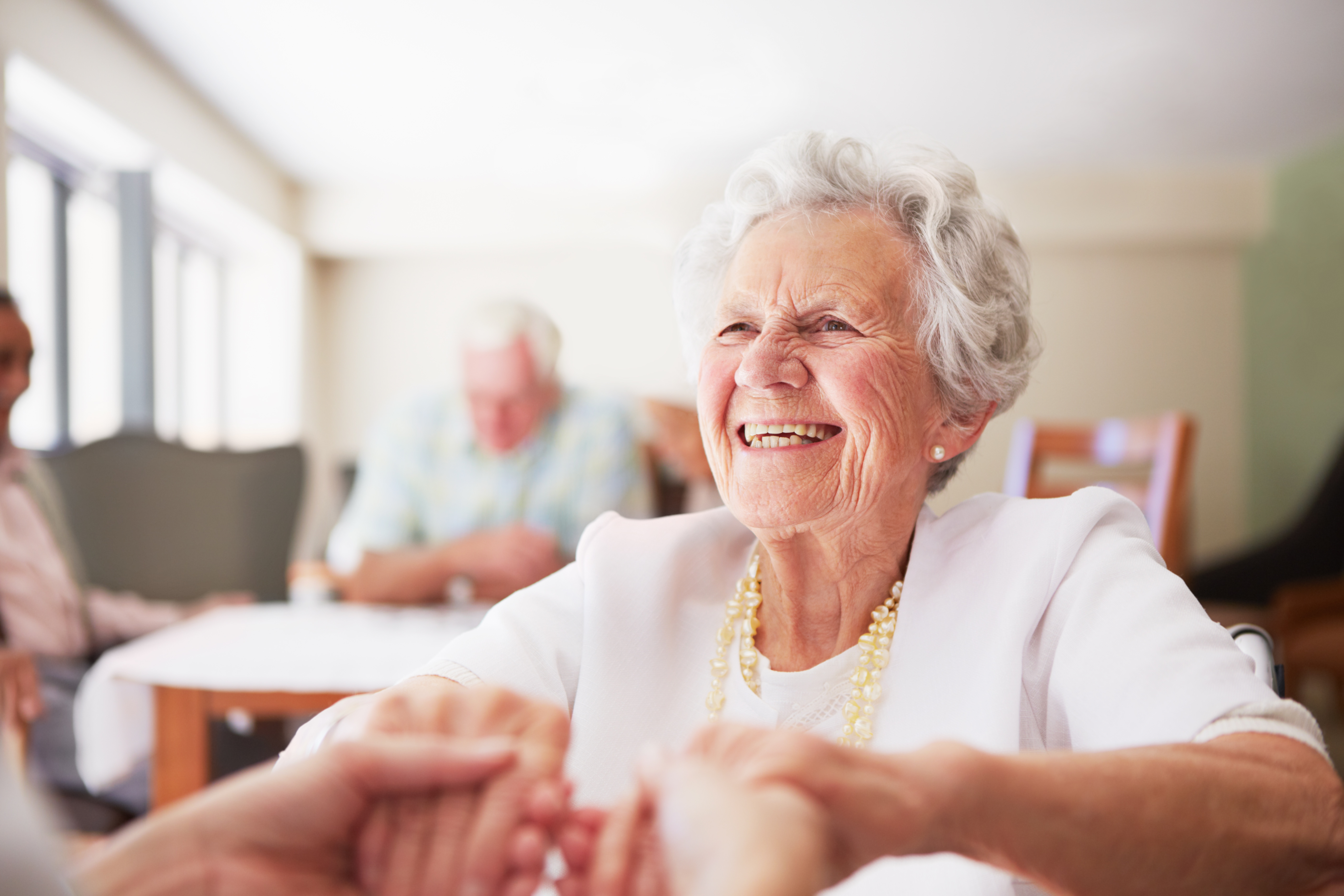 Eine ältere Dame lächelt und ergreift die Hände einer anderen Person